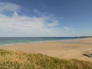 A sandy beach with ocean waves and grassy dunes at Lapwing in Perranporth