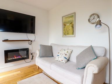 A sitting room with a wall mounted TV a wall clock a floor lamp and a sofa with cushions at Lapwing in Perranporth