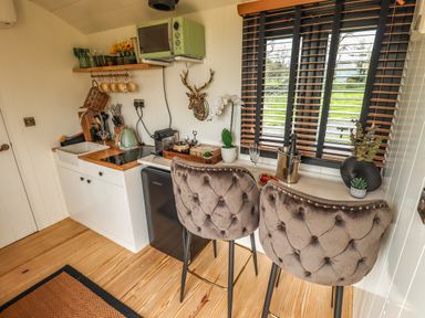 A small kitchen area with a sink stove microwave and two upholstered chairs by a counter with windows at Portland Luxury Glamping in Nottingham