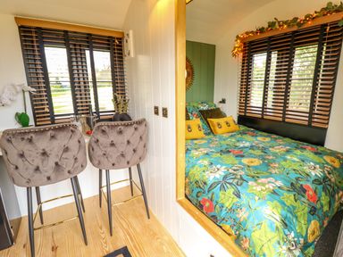 A small bedroom with a floral bedspread next to a breakfast bar with two upholstered chairs at Portland Luxury Glamping in Nottingham