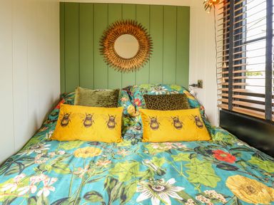 A bed with floral bedding and yellow bee print pillows under a decorative round mirror in a room with green and white walls at Portland Luxury Glamping in Nottingham