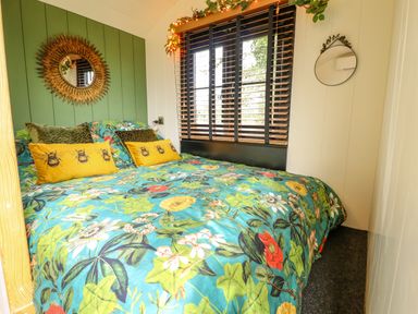 A bedroom with floral bedding green accent wall and two mirrors at Portland Luxury Glamping in Nottingham