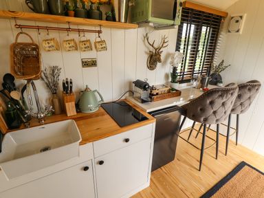 A kitchen area with a sink stove kettle coffee machine and two bar stools at Portland Luxury Glamping in Nottingham