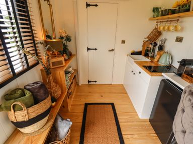 A small kitchen with wooden floor and countertop a black fridge and a basket with blankets at Portland Luxury Glamping in Nottingham