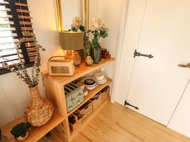 A corner with wooden shelves holding a lamp, radio, toast toaster, bowls, woven baskets, and decorative vases at Portland Luxury Glamping in Nottingham