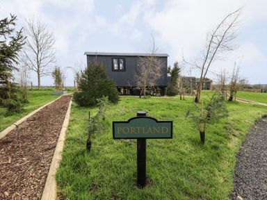 A pathway and grassy area with a sign saying Portland and a small black building in the background at Portland Luxury Glamping in Nottingham