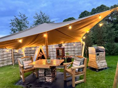 An outdoor seating area with wooden chairs and a table under a canopy with string lights at Portland Luxury Glamping in Nottingham