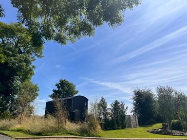 A black wooden cabin surrounded by trees and grass under a blue sky at Portland Luxury Glamping in Nottingham