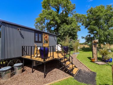 A small grey cabin with a wooden deck and two chairs in a garden with trees at Portland Luxury Glamping in Nottingham