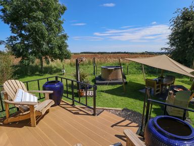 A wooden deck with Adirondack chairs and blue pots overlooking a grassy yard with a hot tub a shaded seating area and barbecue at Portland Luxury Glamping in Nottingham