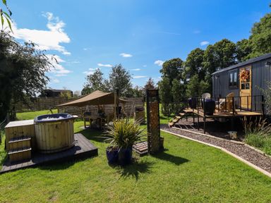 An outdoor space with a hot tub on a wooden platform a tented dining area a shed with stairs and chairs and plants at Portland Luxury Glamping in Nottingham