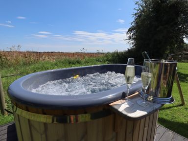 An outdoor hot tub with bubbles and a rubber duck with two glasses of champagne and a bottle in an ice bucket at Portland Luxury Glamping in Nottingham