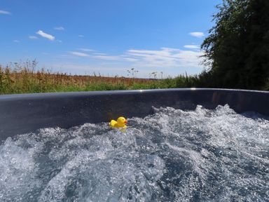 A bubbling hot tub with a yellow rubber duck floating in it outdoors with grass and trees in the background at Portland Luxury Glamping in Nottingham