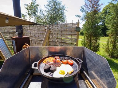 A grill with a full breakfast including eggs, sausages, baked beans, tomatoes, mushrooms, bacon, and black pudding outdoors at Portland Luxury Glamping in Nottingham