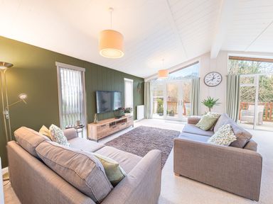 A living room with two sofas a large rug a wall mounted TV and glass doors at Fern Lodge in Allithwaite near Cartmel