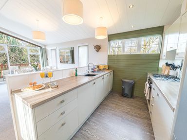 A kitchen with countertop appliances and dining area visible through glass doors at Fern Lodge in Allithwaite near Cartmel