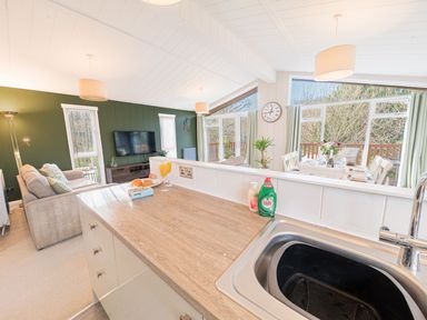An open plan living room and dining area with a kitchen counter and sink in the foreground at Fern Lodge in Allithwaite near Cartmel
