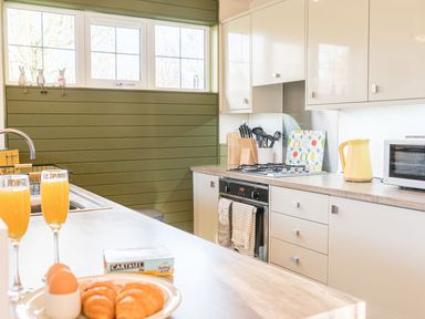 A kitchen with white cabinets a stove and croissants with orange juice on the counter at Fern Lodge in Allithwaite near Cartmel