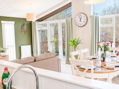 A dining area with a set table and a living room with a sofa and large windows at Fern Lodge in Allithwaite near Cartmel