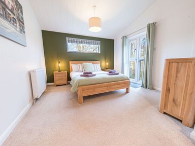 A bedroom with a wooden bed and two bedside tables with lamps at Fern Lodge in Allithwaite near Cartmel