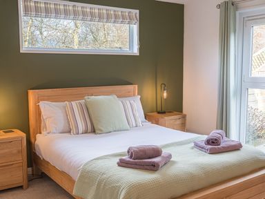 A bedroom with a wooden bed and bedside tables and folded towels on the bed at Fern Lodge in Allithwaite near Cartmel
