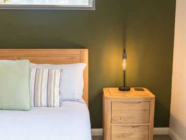 A wooden bed with pillows next to a wooden nightstand with a lamp on a green wall in a bedroom at Fern Lodge in Allithwaite near Cartmel