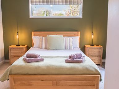 A bedroom with a wooden bed linen towels and bedside tables with lamps at Fern Lodge in Allithwaite near Cartmel
