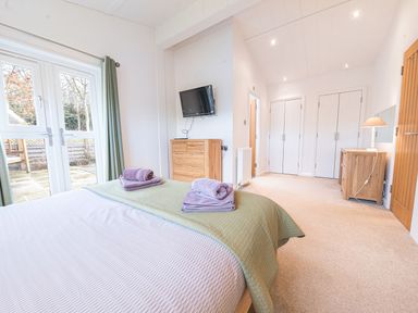 A bedroom with a bed and folded towels near glass doors and wooden furniture at Fern Lodge in Allithwaite near Cartmel
