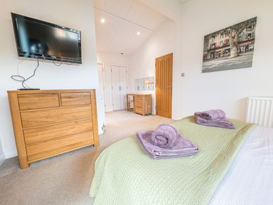 A bedroom with a bed holding folded towels a wooden dresser a wall-mounted TV a door and a dressing table with a mirror at Fern Lodge in Allithwaite near Cartmel