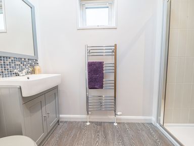 A bathroom with a sink cabinet mirror radiator with a purple towel window and a shower enclosure at Fern Lodge in Allithwaite near Cartmel