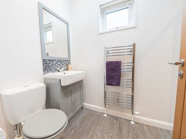 A bathroom with a toilet sink with mirror and towel rack with purple towel at Fern Lodge in Allithwaite near Cartmel