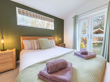 A bedroom with a bed pillows towels wooden bedside tables and a window overlooking a garden at Fern Lodge in Allithwaite near Cartmel