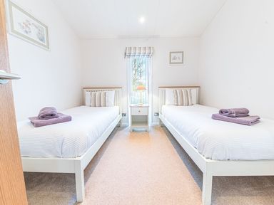 A bedroom with two single beds each with white bedding and purple towels a bedside table with a lamp between the beds at Fern Lodge in Allithwaite near Cartmel