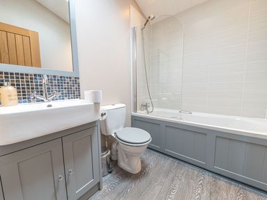 A bathroom with a sink, toilet, and bathtub with shower at Fern Lodge in Allithwaite near Cartmel