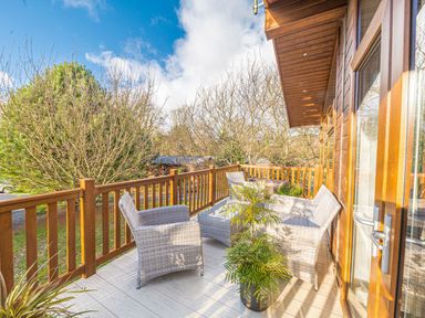 An outdoor wooden balcony with wicker chairs a table and potted plants at Fern Lodge in Allithwaite near Cartmel