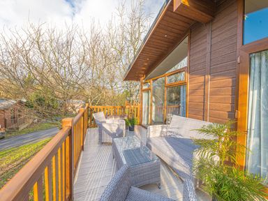 An outdoor wooden deck with wicker furniture including chairs a sofa and a glass table at Fern Lodge in Allithwaite near Cartmel