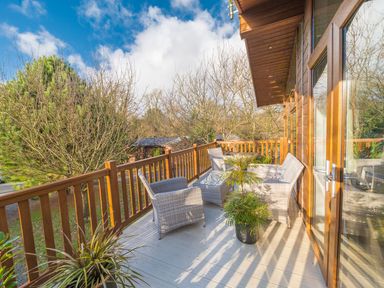 A balcony with wicker chairs a glass table and potted plants at Fern Lodge in Allithwaite near Cartmel