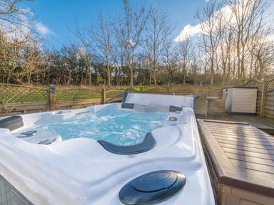 An outdoor hot tub with bubbling water surrounded by wooden fencing and trees at Fern Lodge in Allithwaite near Cartmel