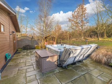 An outdoor patio area with a hot tub a storage box wooden fencing and trees at Fern Lodge in Allithwaite near Cartmel