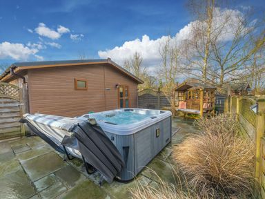 An outdoor patio with a hot tub and a wooden swing seat surrounded by wooden fencing at Fern Lodge in Allithwaite near Cartmel