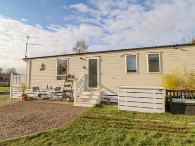 A single-story mobile home with a small patio table and chairs and potted plants outside at 46 Willowburn in Felton