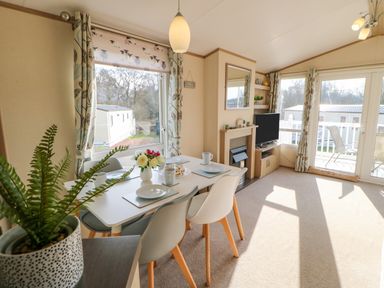 A dining area with a table set for four next to large windows and a living space with a TV and fireplace at 46 Willowburn in Felton