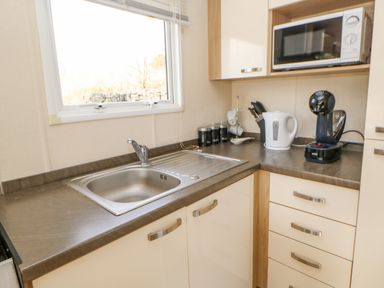 A kitchen countertop with a stainless steel sink under a window a microwave kettle coffee machine and canisters at 46 Willowburn in Felton