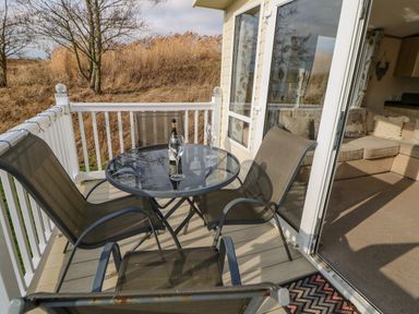 A balcony with a glass table holding a bottle and two glasses and three chairs outside a living room at 46 Willowburn in Felton