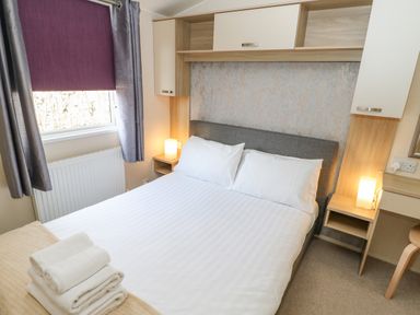 A bedroom with a double bed two bedside tables with lamps towels on the bed and a window with curtains at 46 Willowburn in Felton