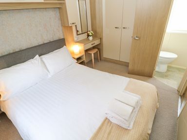A bedroom with a double bed towels on bed a small dressing table with a stool wardrobe and a door leading to a bathroom at 46 Willowburn in Felton