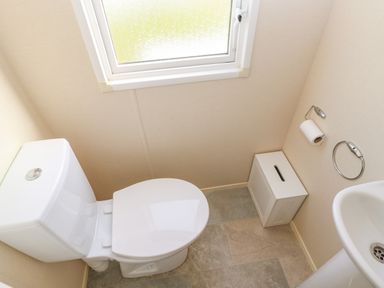 A toilet, a small window, a tissue box on the floor, a toilet paper holder, and a sink in a bathroom at 46 Willowburn in Felton