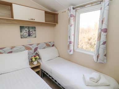 A bedroom with two single beds a window and floral curtains at 46 Willowburn in Felton