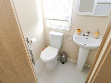 A small bathroom with a toilet a sink a mirror and a window at 46 Willowburn in Felton