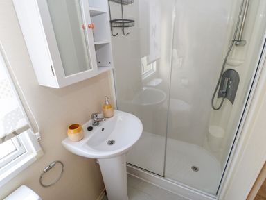 A bathroom with a white sink cabinet a shower cubicle and a window at 46 Willowburn in Felton